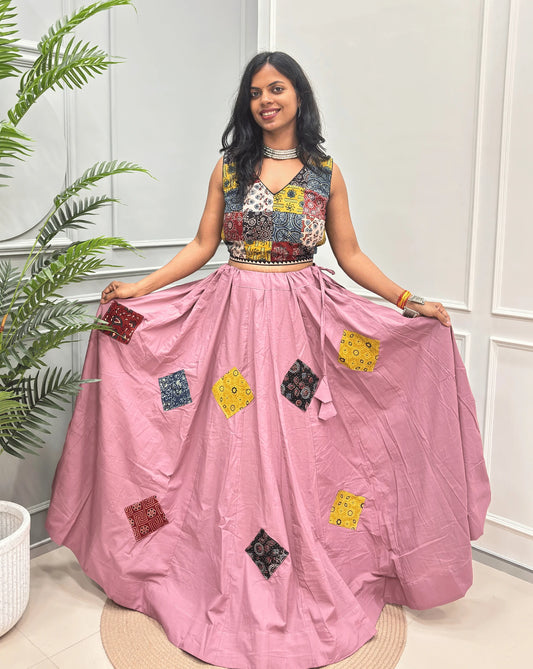 Onion Pink Women's Ajrakh Pure Cotton Skirt, featuring a multicolor patchwork & printed sleeveless top and a voluminous pink skirt adorned, set against a white paneled wall with a potted plant.