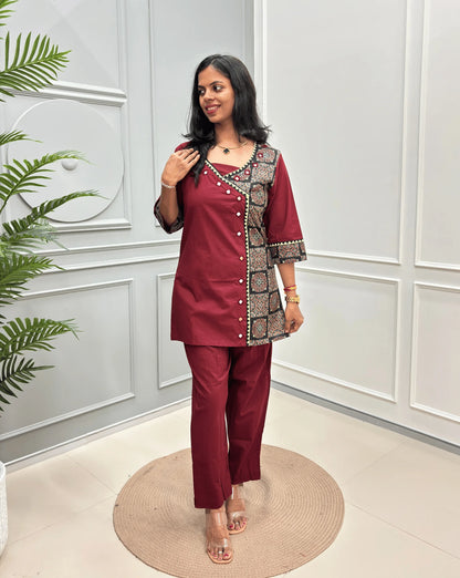Red Women's Ajrakh Pure Cotton 2-peice Co-Ord set with a Ajrakh printed panel on the front & Sleeves, Angrakha Patterned on front, standing on a round woven rug in a modern room with white paneled walls.