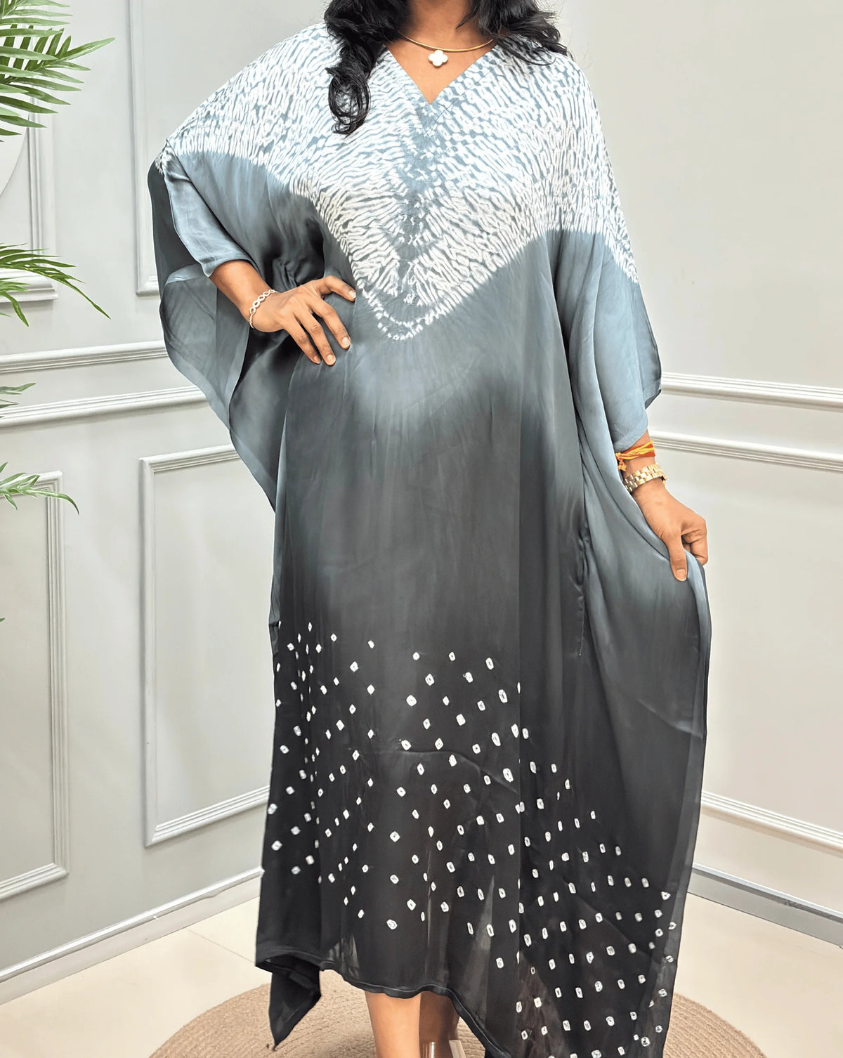Closed-up View of Grey Women's Ajrakh Pure Modal Silk Shibori Kaftan Featured with Long-length, with a 3 shades of Grey with ajrakh print on chest & Bandhani Small dots with white on Bottom Along with Full Sleeves & Free Size, standing on a round woven rug in front of a white paneled wall.