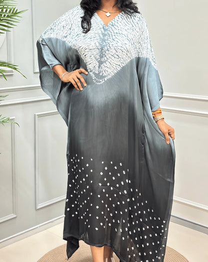 Closed-up View of Grey Women's Ajrakh Pure Modal Silk Shibori Kaftan Featured with Long-length, with a 3 shades of Grey with ajrakh print on chest & Bandhani Small dots with white on Bottom Along with Full Sleeves & Free Size, standing on a round woven rug in front of a white paneled wall.