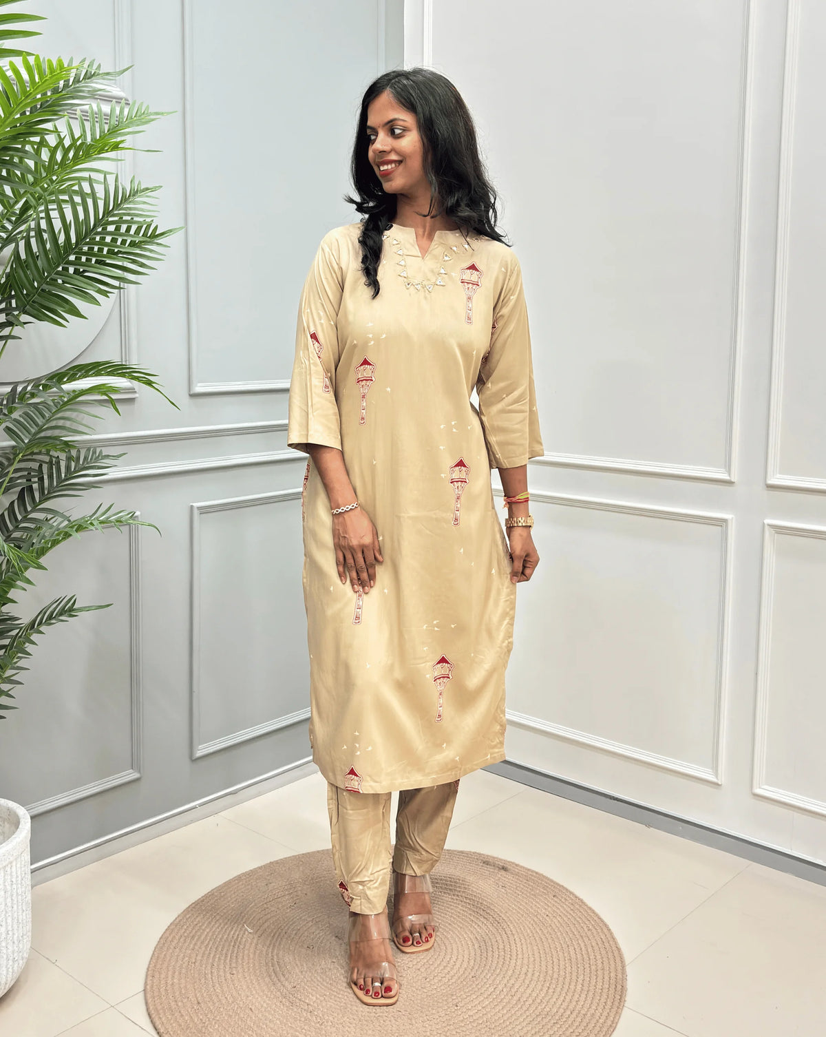 Beige Women's Ajrakh  Vegetable Dyed Cotton Long Co-Ord set with small red and green embroidered details, along with matching pants, standing in a modern room with white paneled walls and a potted plant.