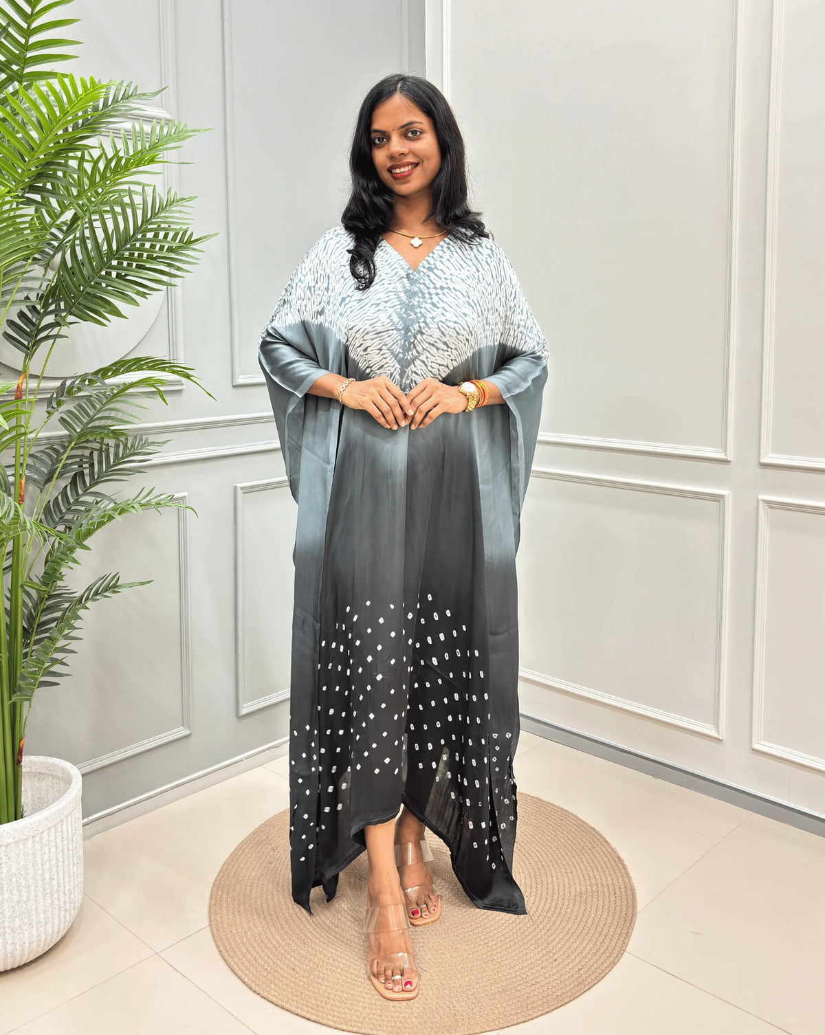Grey Women's Ajrakh Pure Modal Silk Kaftan with a 3 shades of Grey with ajrakh print on chest & Bandhani Small dots with white on Bottom, standing on a round woven rug in front of a white paneled wall.