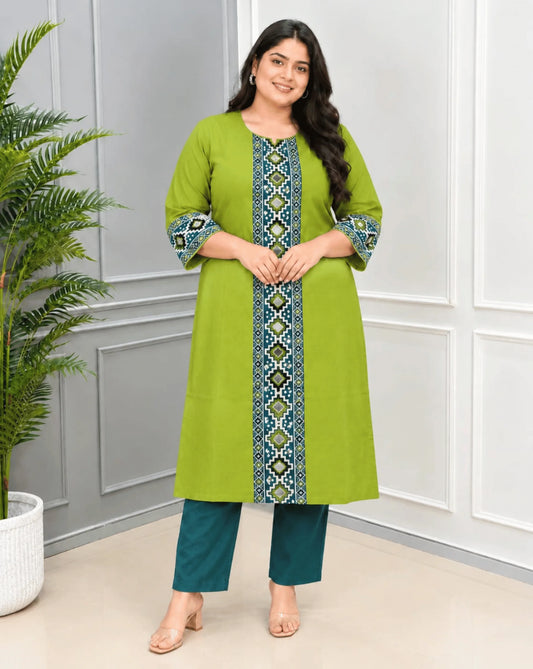 Light Green Women's Ajrakh Vegetable dyed plant based Cotton Long Kurti with a  Ajrakh & patola print on front & sleeves, standing in front of white & grey wall , green planted pot on the left.
