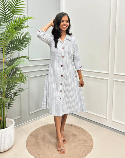Grey Women's Ajrakh A-line Pure Cotton Long Kurti with an Ajrakh Strip Print on abstract of Grey, White, standing on a round woven rug in front of a light gray paneled wall with a potted plant.