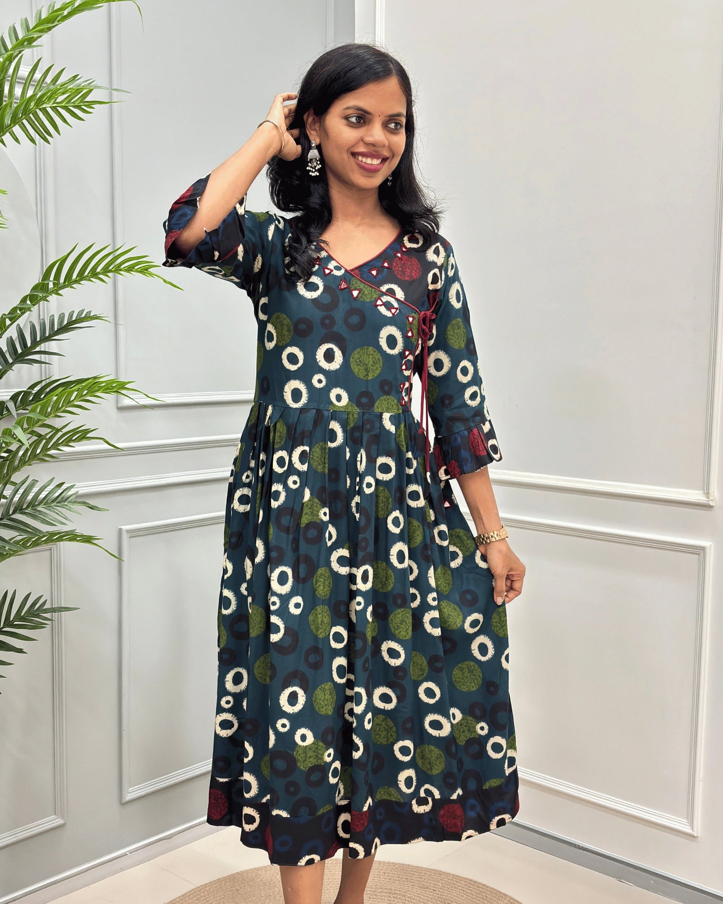 Green women's vegetable dyed plant based cotton long kurti front-view with a colorful white, green & black circle print,  and red floral accents, set against a white paneled wall with a green plant on the left.