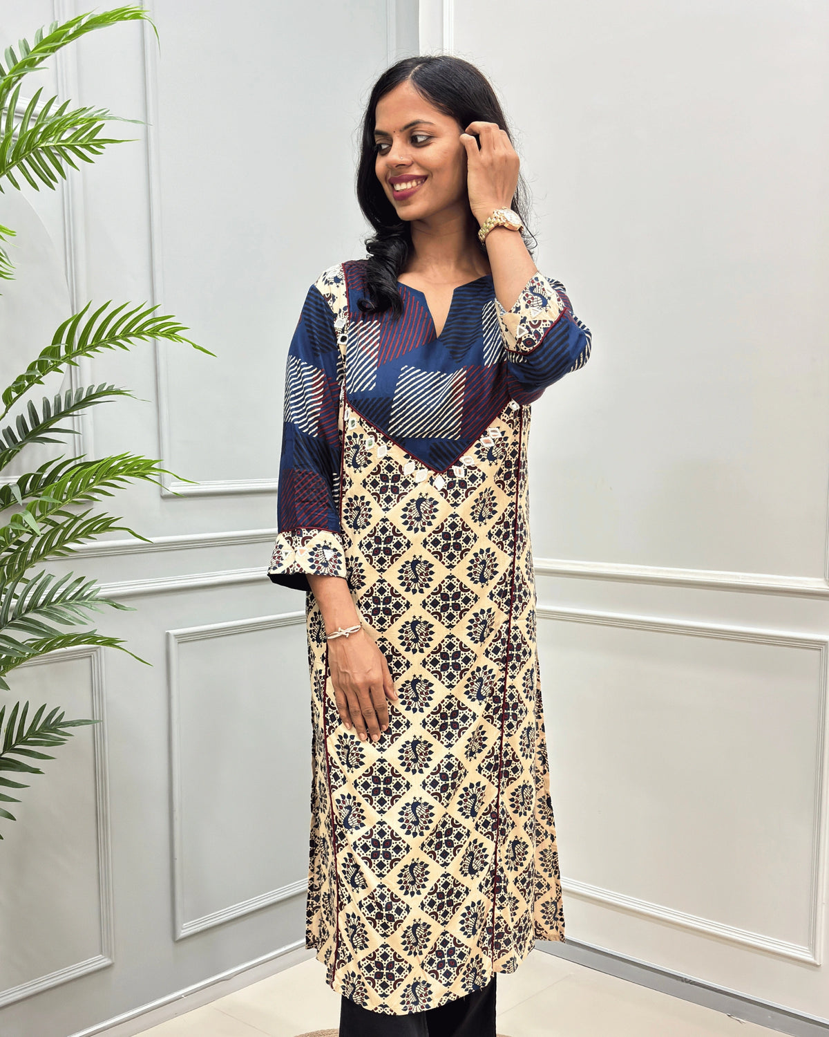 front side view of Beige cotton long kurti with Hand-mirror work on V-shaped yoke on front and sleeves, red colour pie-pin on front , peacock print on Beige base .