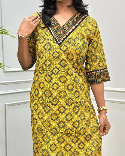 Close-up of Green and Yellow Hand-block Ajrakh pure cotton Long-kurta with a Ajrakh geometric pattern, featuring a V-neckline and patterned sleeve cuffs, standing against a white paneled wall