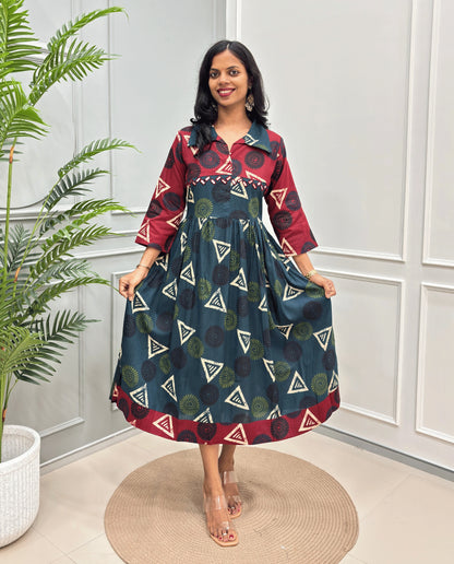 Bottle-Green Women's Ajrakh Vegetable dyed plant based Cotton Long-Kurti with a Red neck, bottom and cuffs, and a green-colored dress featuring a geometric pattern of triangles and spiral in green, black, and beige, standing on a round woven rug in front of a white paneled wall with a green potted plant on the left.