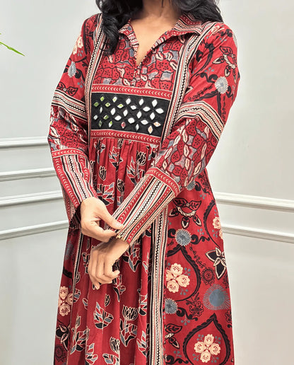 Close-up of handcrafted mirror work on red Ajrakh cotton kurti along with Ajrakh printed Sleeves detail on long kurti , standing against a white paneled wall.
