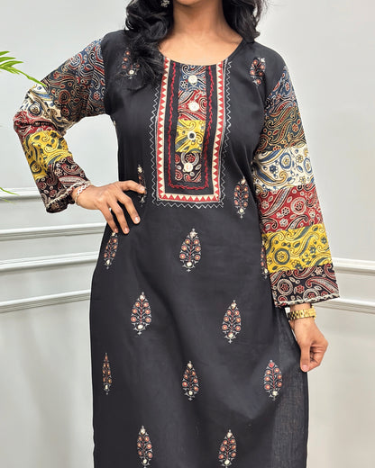 Close-up of Green Rayon Cotton Co-Ord Set with intricate multicolor printed patterns on Full-sleeves, neckline with block , and Hand-mirror motifs on the front, standing against a light gray paneled wall.