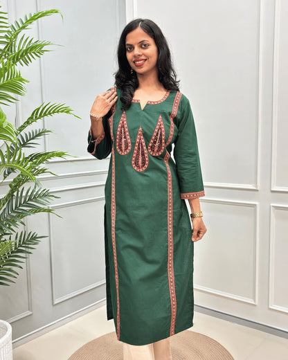 Green Women's Ajrakh Pure Cootn Long-kurti with Beige and Red Ajrakh print with Palm-leaf detailing , paired with beige pants, standing in a room with a potted plant and paneled wall