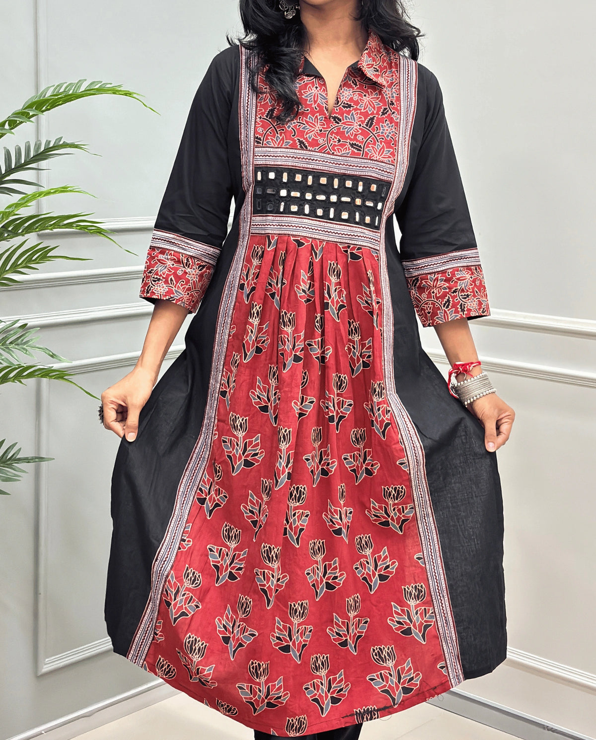 Close-up of Red Ajrakh plant based cotton long-kurti consisting a red colour and a matching Black floral printed frill.  black and grey printed yoke panel, three-quarter sleeves with matching prints, and a hand-mirror work waistband, Collar V-neck .