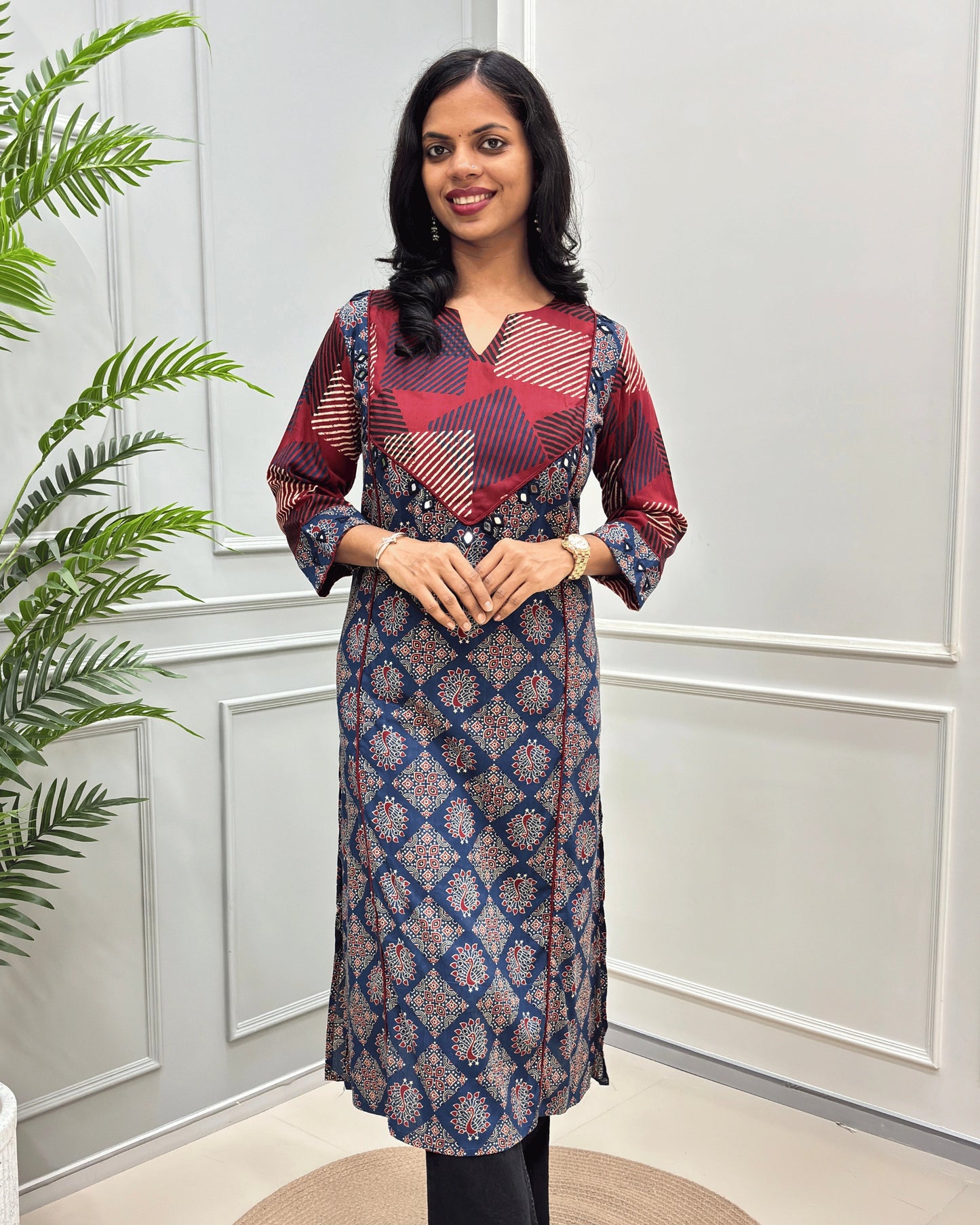 front side view of blue cotton long kurti with Hand-mirror work on V-shaped yoke on front and sleeves, red colour pie-pin on front , peacock print on blue base .