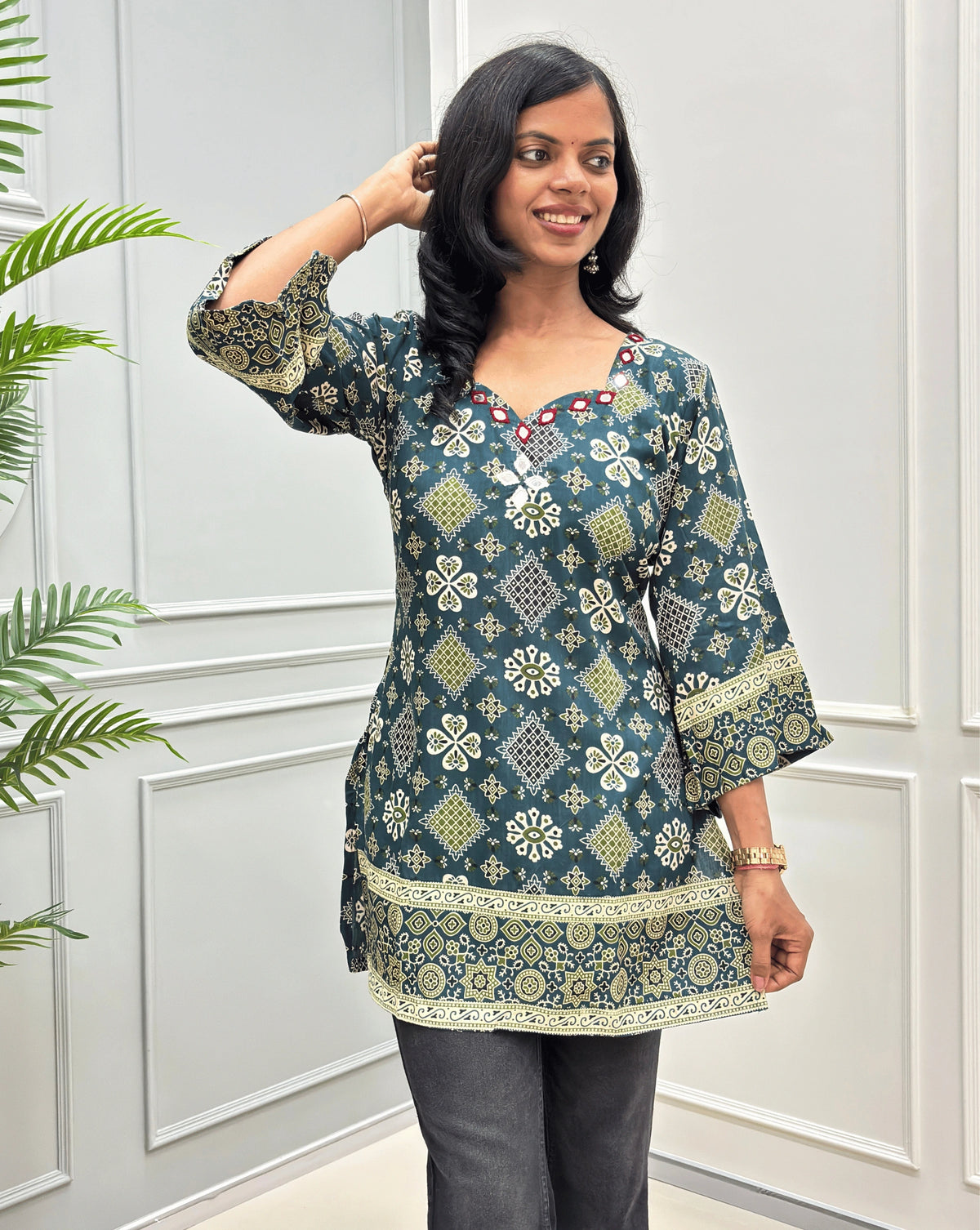 Dark Green women's cotton Ajrakh Short kurti front view with mirror work with white & yellow geometric patterns, bottom paired with dark black pant.