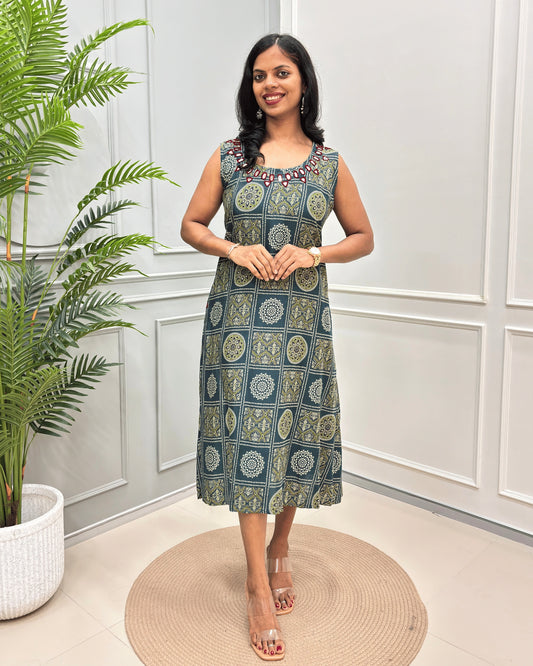 Green Women's Vegetable dyed Plant based Cotton Long-kurti with a green and beige geometric pattern and Hand-Mirror Work on neckline, standing in a decorated room with a potted plant and paneled walls.