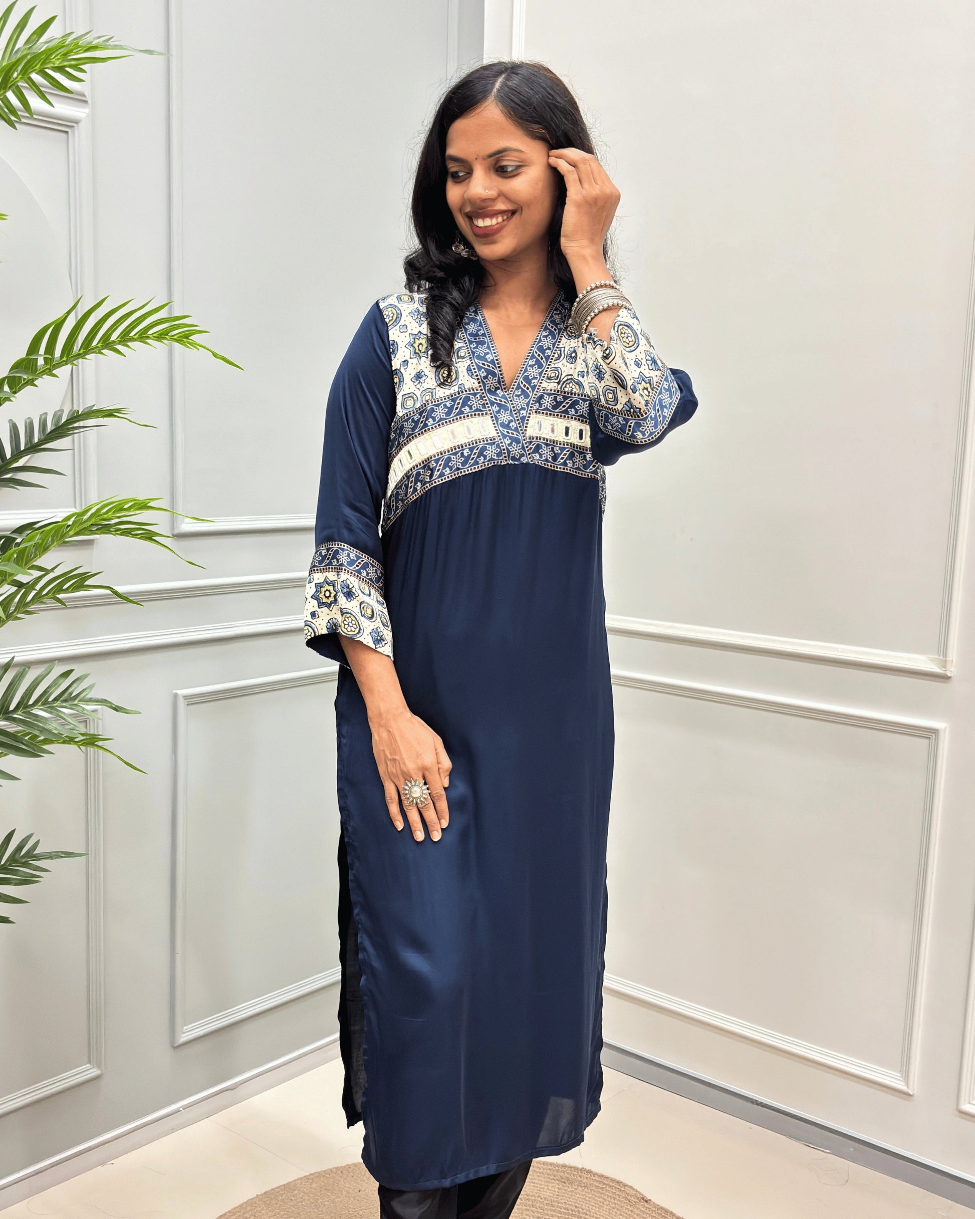 Front view of Navy-Blue women's Ajrakh Modal Silk Long lurti featured with white base & ajrakh print on neck & cuffs , hand-mirror work on chest standing in a white paneled room.