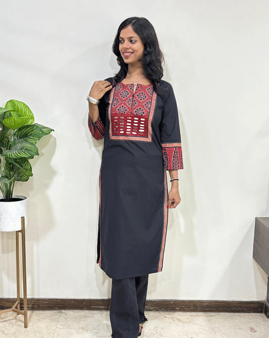 Black women's Hand-block Ajrakh Pure Cotton Long Kurti with red and Black geometric embroidery on the chest and cuffs, paired with matching dark pants, standing in front of a plain white wall.